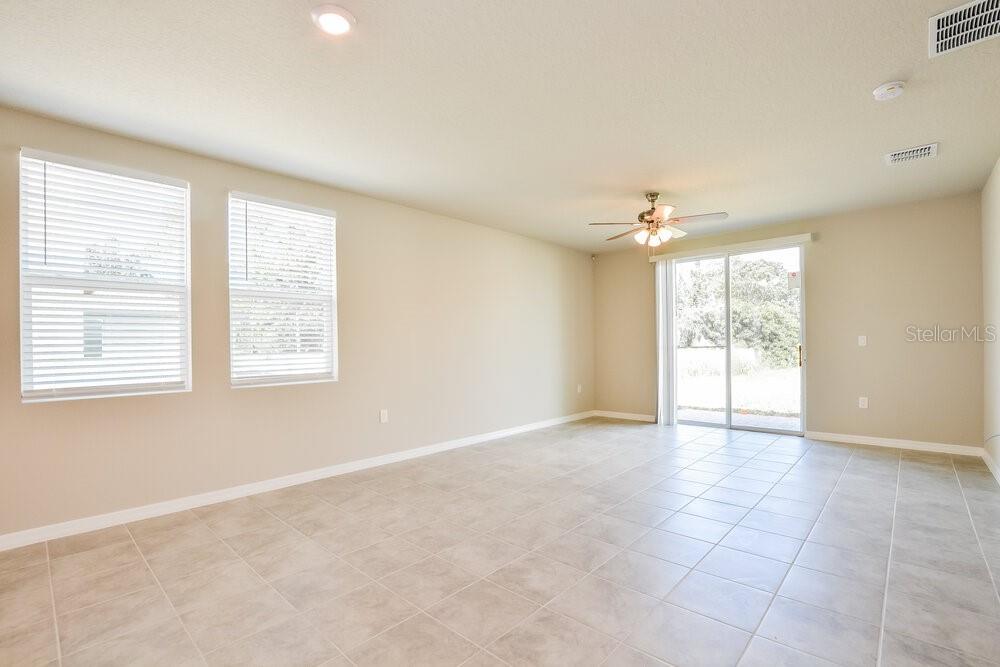 An empty living room features beige walls, tile flooring, a ceiling fan, and sliding doors — 5247 MEREDREW LANE, ST CLOUD, FL