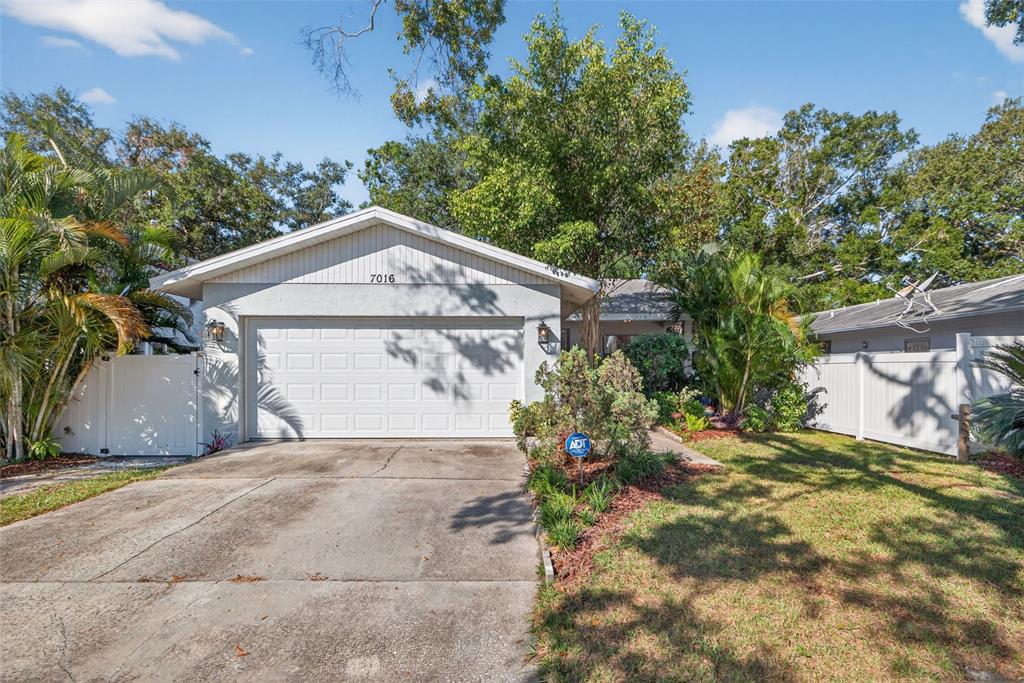 A single-story house with a white garage door, concrete driveway, and surrounding trees — 7016 2ND STREET N, ST PETERSBURG, FL