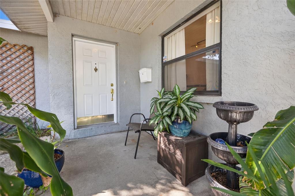 A covered concrete front porch features a white door, a window, and several potted plants — 7016 2ND STREET N, ST PETERSBURG, FL