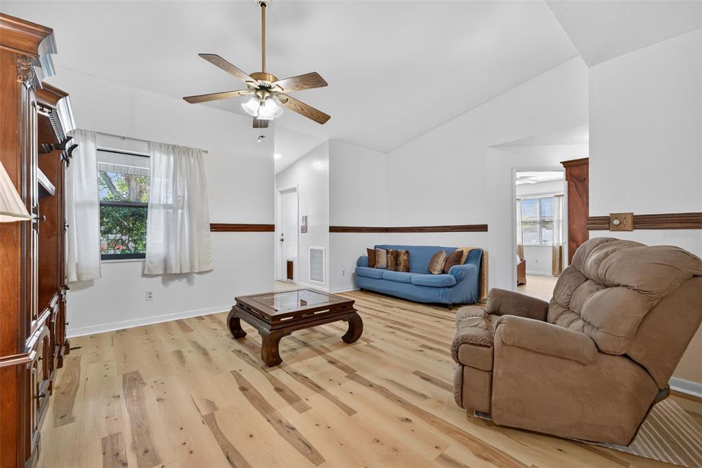 A living room features light wood flooring, a blue sofa, a recliner, and a ceiling fan — 7016 2ND STREET N, ST PETERSBURG, FL