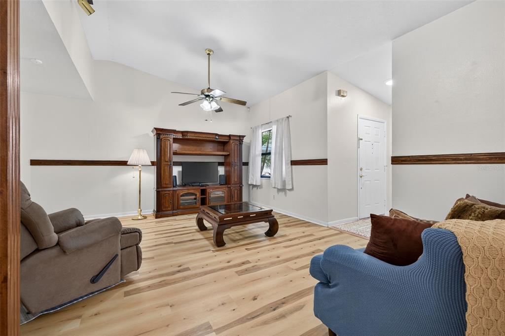A living room features light wood-look flooring, a wooden entertainment center, and a ceiling fan — 7016 2ND STREET N, ST PETERSBURG, FL
