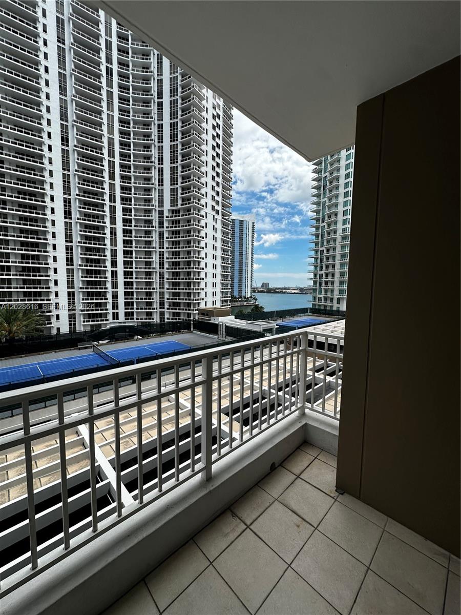 A balcony with tiled flooring overlooks a tennis court, tall residential towers, and the water — 801 Brickell Key Blvd # 906, Miami FL 33131, MIAMI, FL
