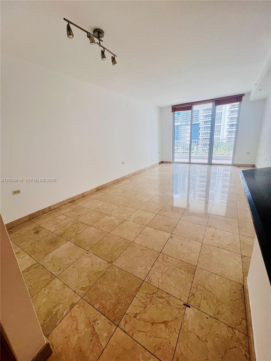 An empty room features beige tile flooring, white walls, a track light, and a balcony — 801 Brickell Key Blvd # 906, Miami FL 33131, MIAMI, FL