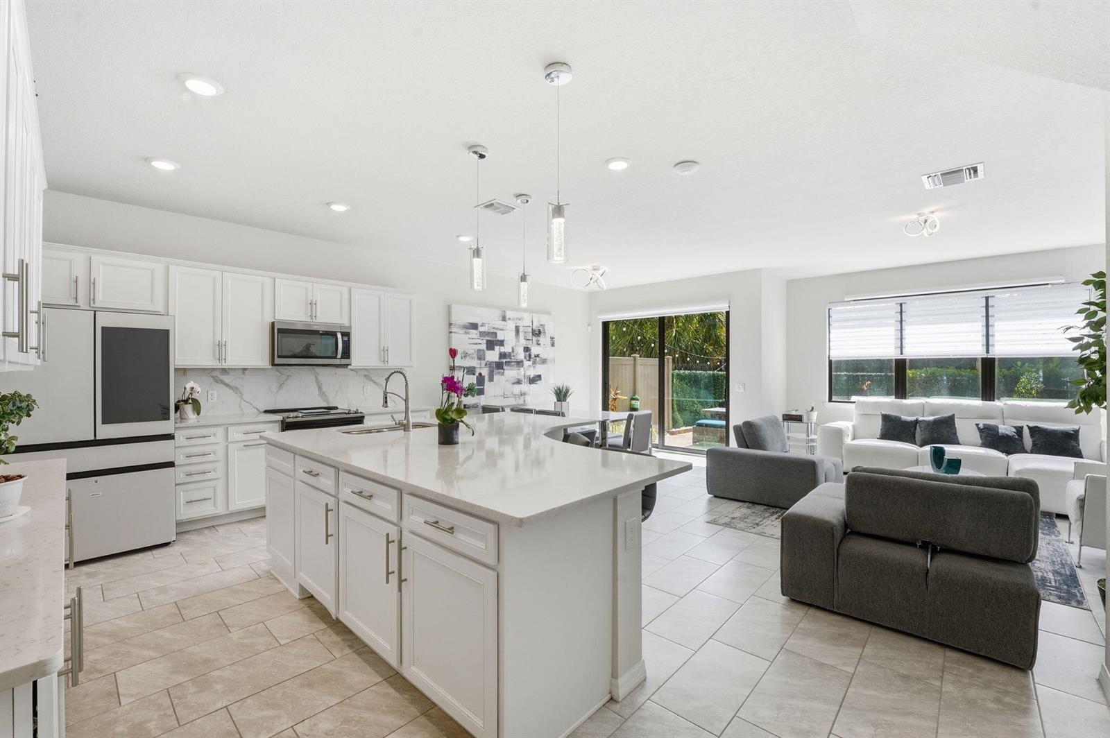 A bright open-concept kitchen and living area featuring white cabinetry, a large island, and tile — 4802 Blistering Way, Lake Worth FL 33467, LAKE WORTH, FL