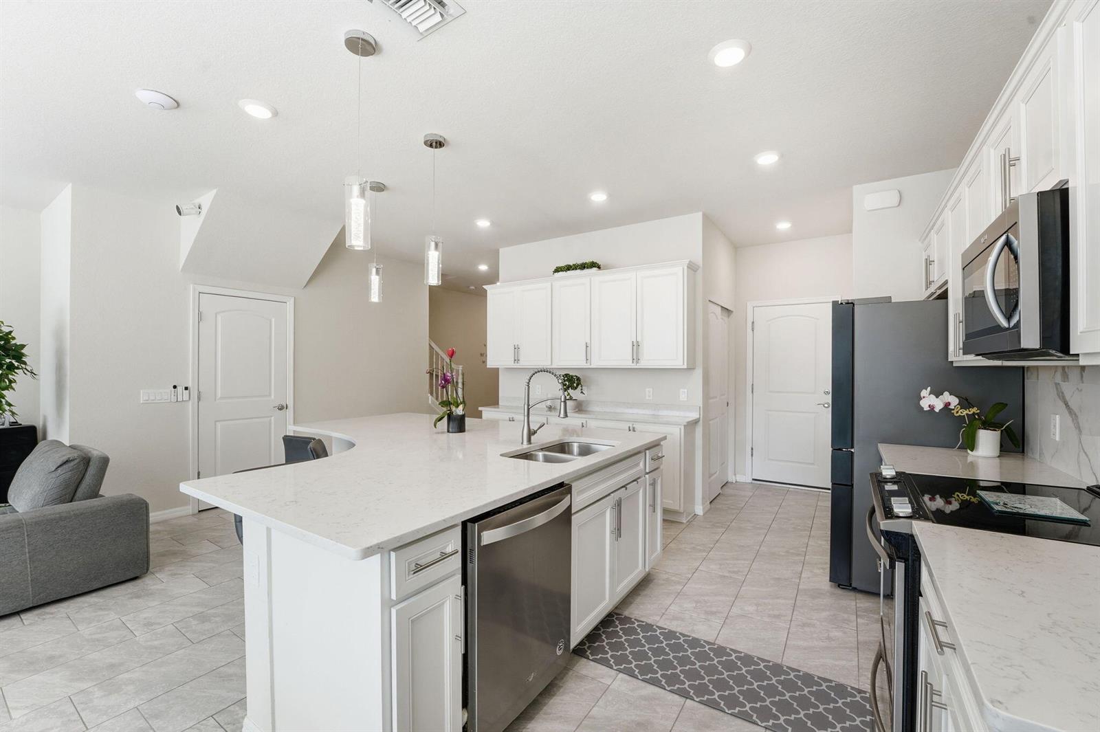 A modern kitchen features white cabinetry, a large quartz island, and stainless steel appliances — 4802 Blistering Way, Lake Worth FL 33467, LAKE WORTH, FL