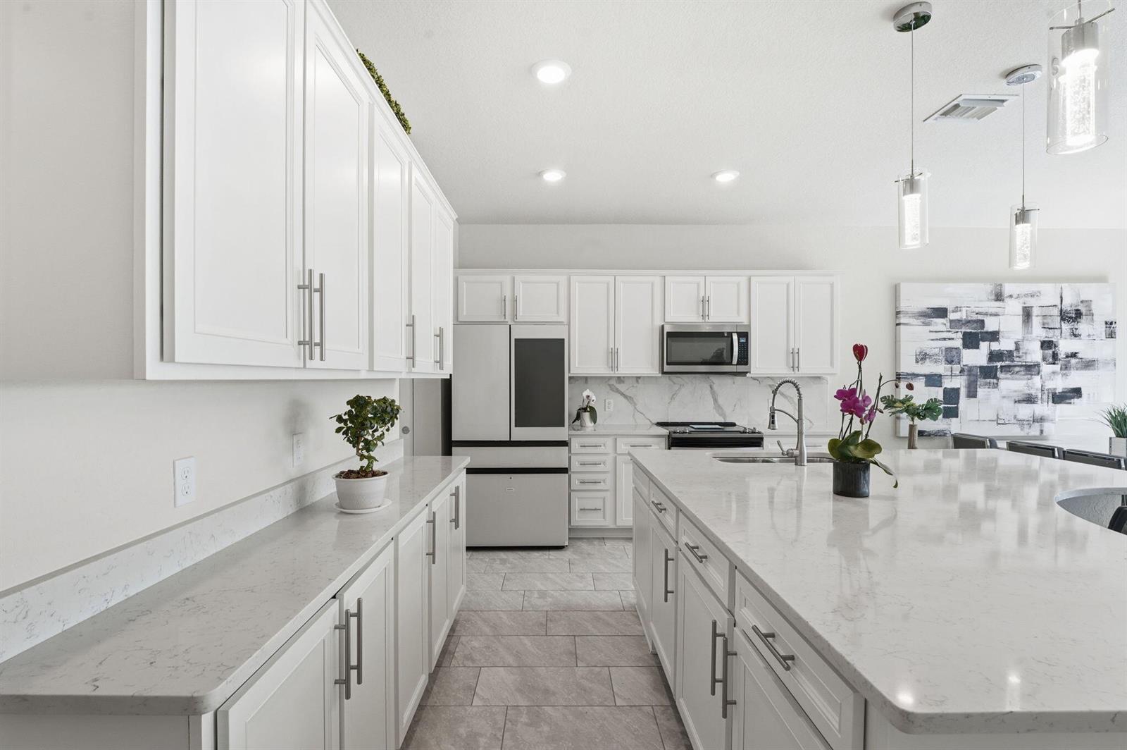 A modern kitchen features white cabinetry, quartz countertops, a large island, and stainless steel appliances — 4802 Blistering Way, Lake Worth FL 33467, LAKE WORTH, FL