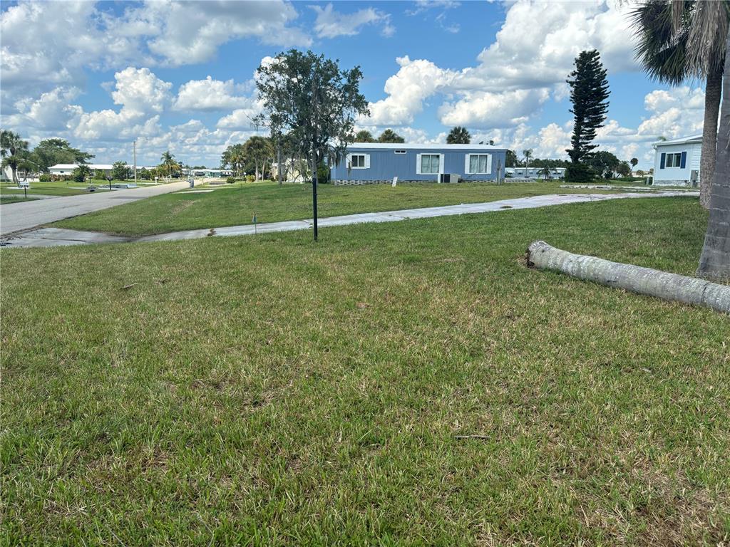 A grassy lot with a fallen palm tree trunk in the foreground and a blue house — 1533 BLUE HERON DRIVE, ENGLEWOOD, FL