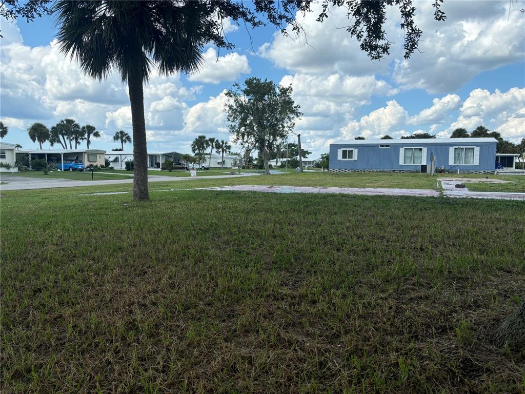 A grassy lot with a concrete pad sits next to a blue mobile home — 1533 BLUE HERON DRIVE, ENGLEWOOD, FL