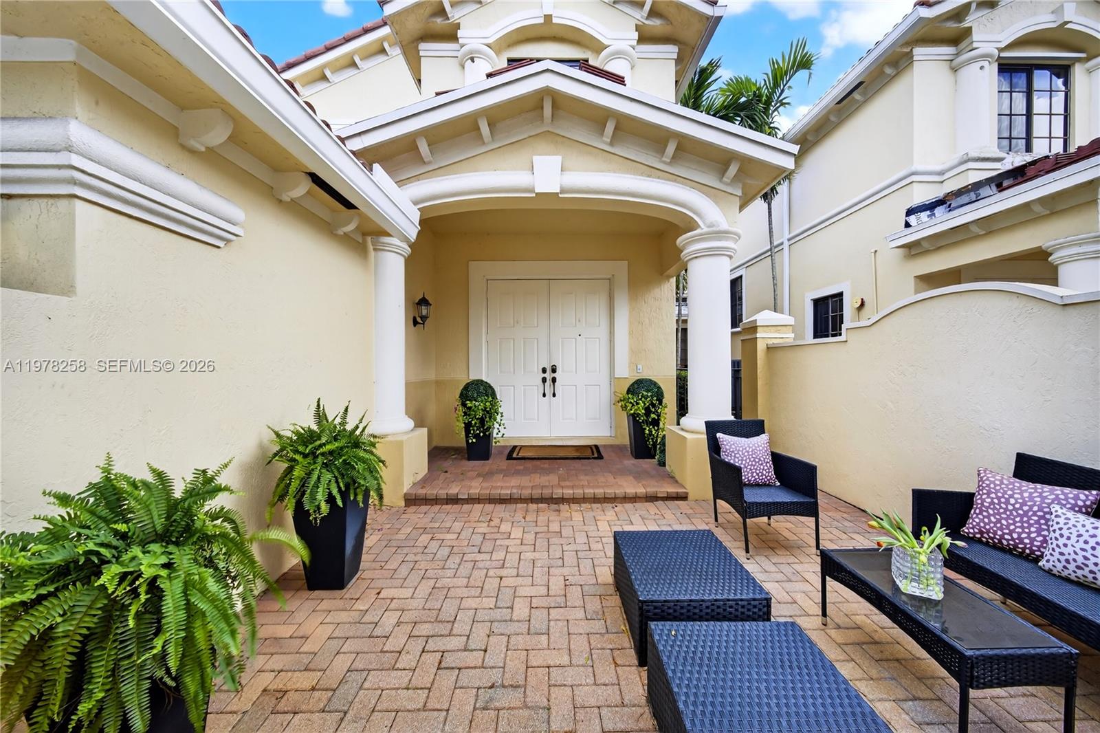 A paved courtyard leads to the white double-door entrance of a beige stucco house — 1506 Passion Vine Cir # 3, Weston FL 33326, WESTON, FL