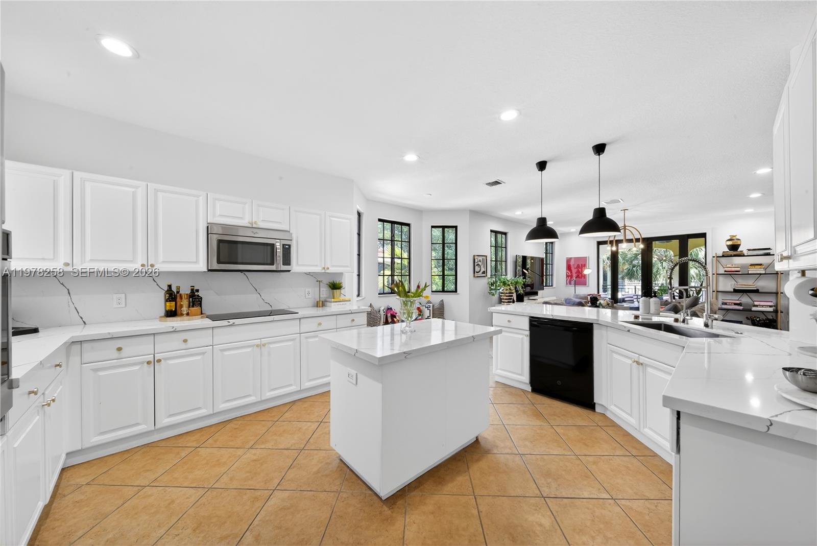 A white kitchen features a central island, marble-style countertops, and brown tile flooring — 1506 Passion Vine Cir # 3, Weston FL 33326, WESTON, FL
