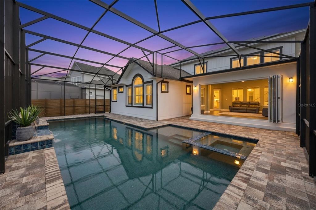 A swimming pool and spa are enclosed within a screened lanai behind a modern house — 14160 ELIOT AVENUE, ORLANDO, FL