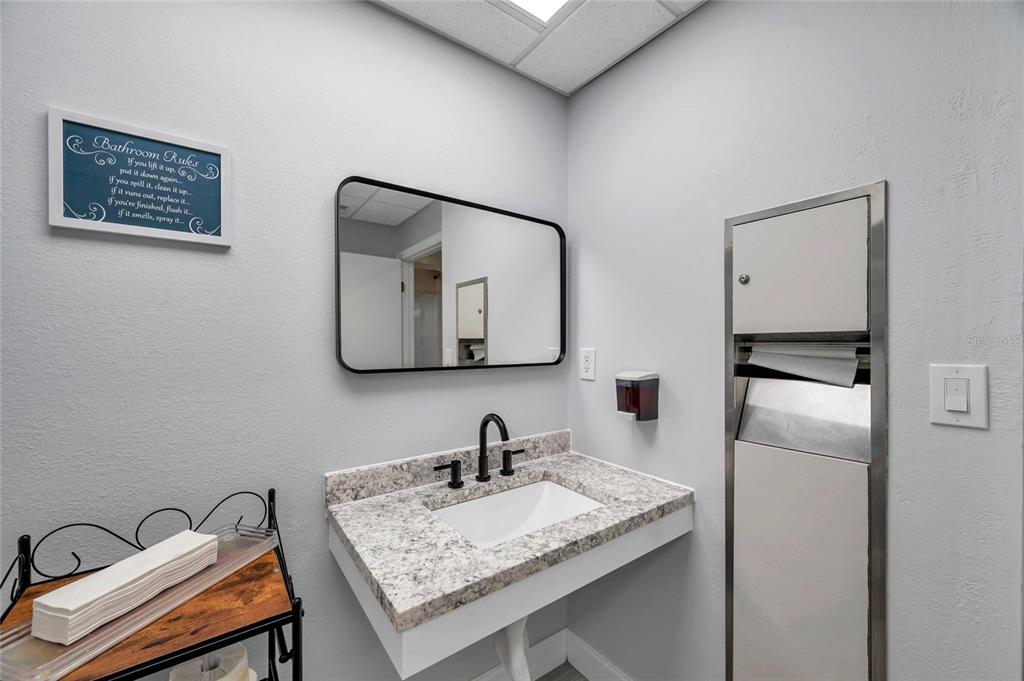 A bathroom features a granite-topped vanity, a rectangular mirror, and a built-in paper towel dispenser — 2401 W BAY DRIVE UNIT 410, LARGO, FL