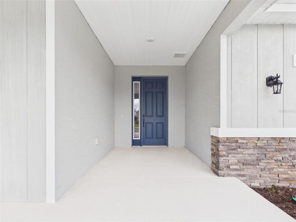 A covered front porch features a blue front door with a side window and stone siding — 5717 SW 71ST COURT, OCALA, FL