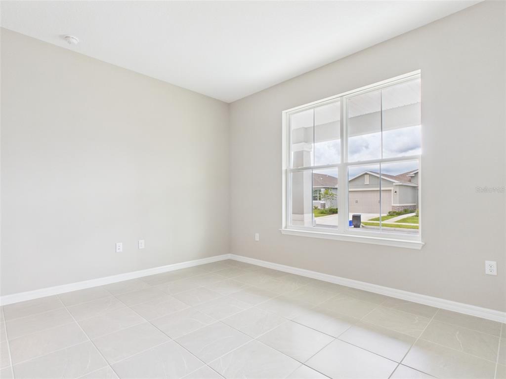 An empty room with light-colored tile flooring, neutral walls, and a large window — 5717 SW 71ST COURT, OCALA, FL