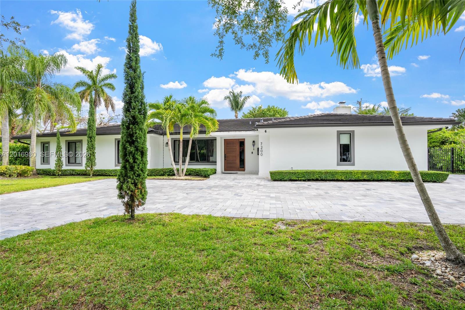 A single-story white house with a paved driveway and palm trees under a blue sky — 7200 SW 107th Ter, Pinecrest FL 33156, PINECREST, FL