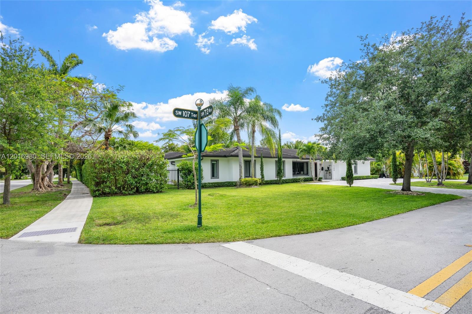 A single-story white house sits behind a green lawn at a street corner intersection — 7200 SW 107th Ter, Pinecrest FL 33156, PINECREST, FL