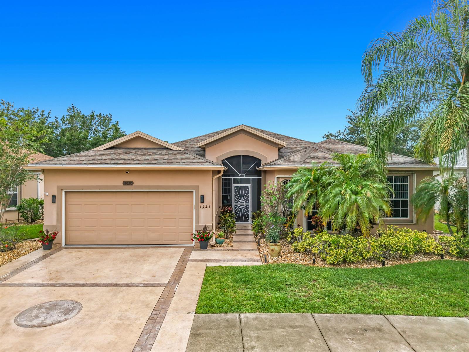 A single-story tan house with a two-car garage, arched entryway, and a palm tree — 1343 Shoreline Circle, Sebastian FL 32958, SEBASTIAN, FL