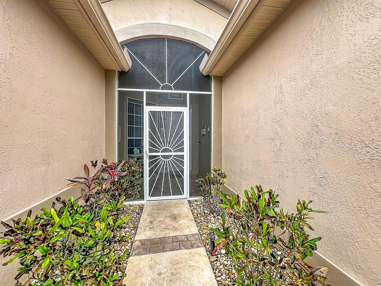 A beige stucco home entrance features a white sunburst screen door and landscaped gravel beds — 1343 Shoreline Circle, Sebastian FL 32958, SEBASTIAN, FL