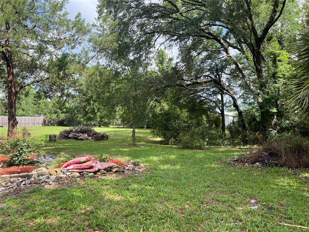 A grassy backyard features a pile of brush, scattered landscaping materials, and mature trees — 9510 SW 94TH TERRACE, GAINESVILLE, FL
