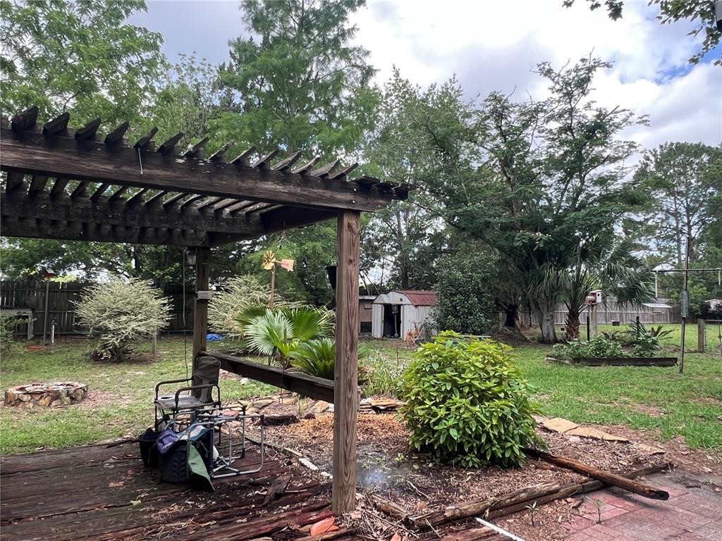 A backyard features a wooden pergola, a small metal shed, and various trees and plants — 9510 SW 94TH TERRACE, GAINESVILLE, FL