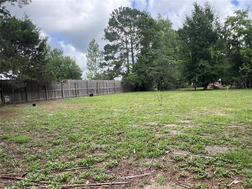 A large, grassy backyard features a wooden privacy fence and several mature trees — 9510 SW 94TH TERRACE, GAINESVILLE, FL