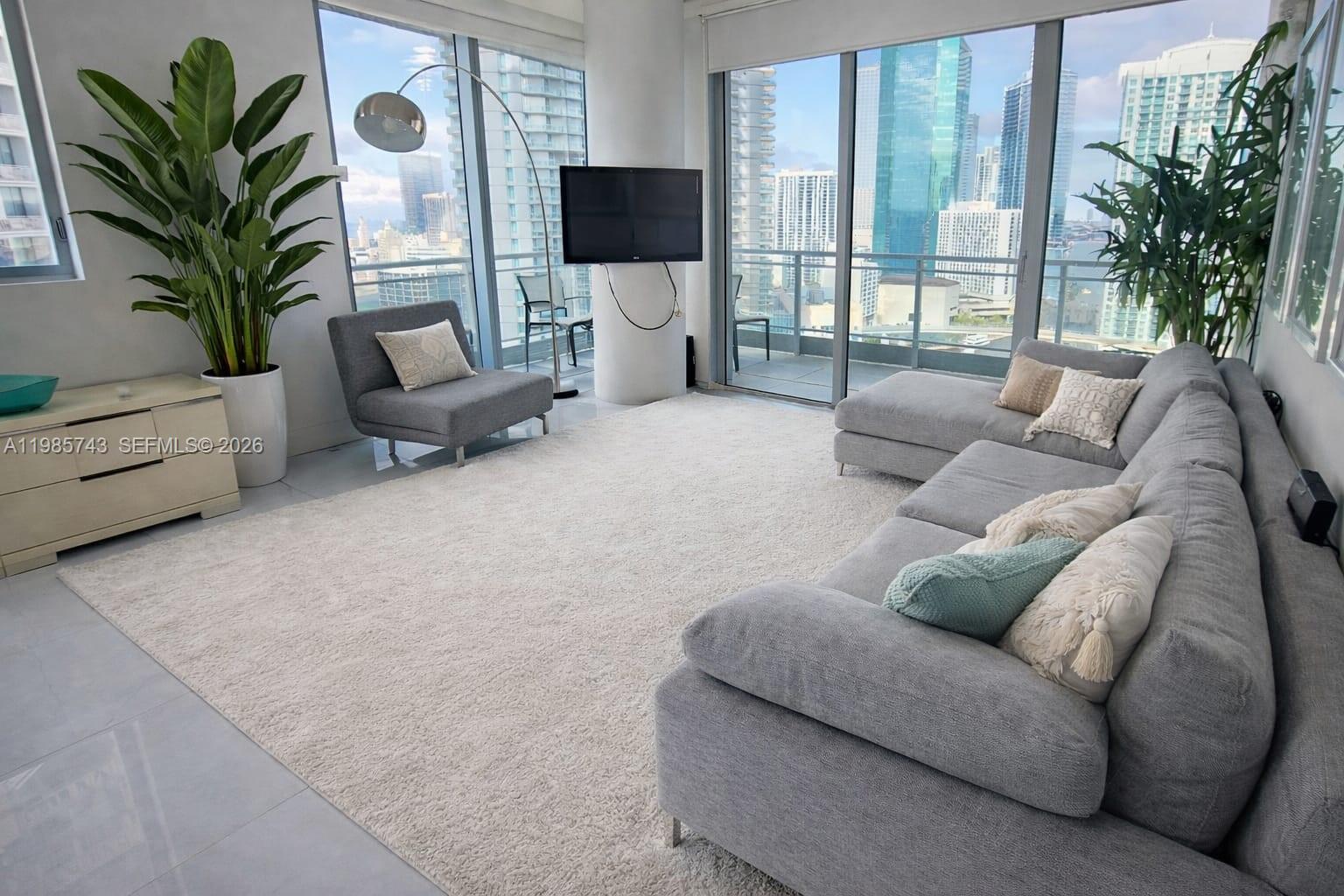 A modern living room features a grey sectional sofa, floor-to-ceiling windows, and city views — 92 SW 3rd St # 2510, Miami FL 33130, MIAMI, FL