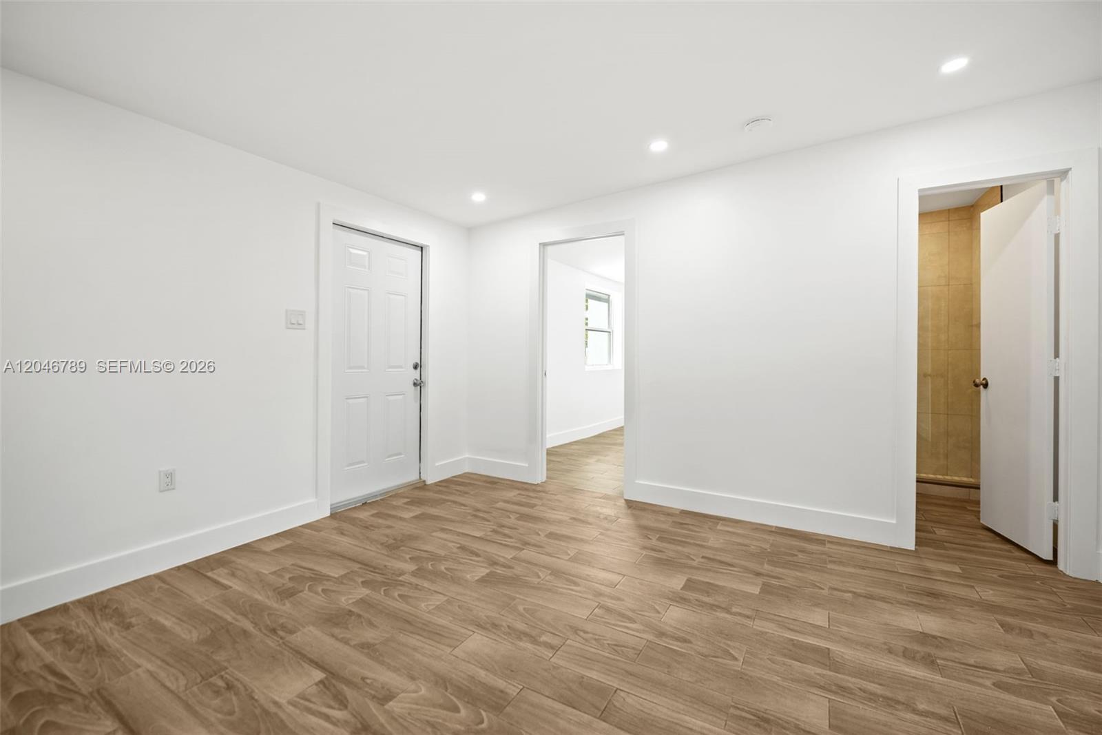 A room with white walls, wood-look tile flooring, a door, and an open doorway — MIAMI, FL