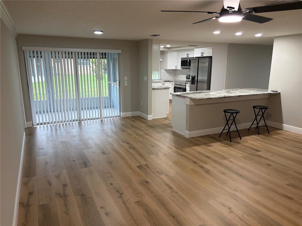 An open-concept living area features light wood flooring, a kitchen island, and sliding glass doors — 12302 FIELDSTONE LANE, HUDSON, FL