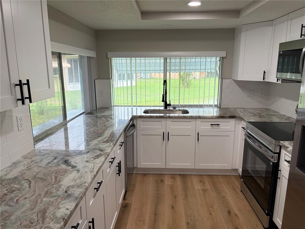 A kitchen features white cabinets, granite countertops, stainless steel appliances, and wood-look flooring — 12302 FIELDSTONE LANE, HUDSON, FL