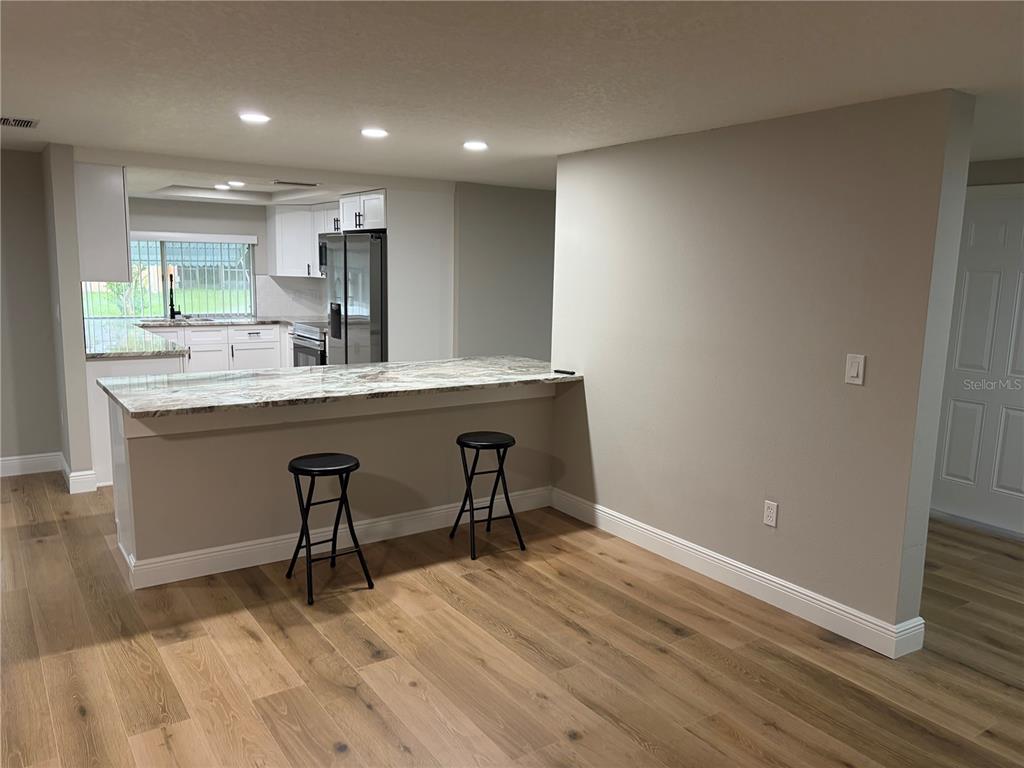 A kitchen features white cabinets, granite countertops, a breakfast bar with two stools, and wood flooring — 12302 FIELDSTONE LANE, HUDSON, FL
