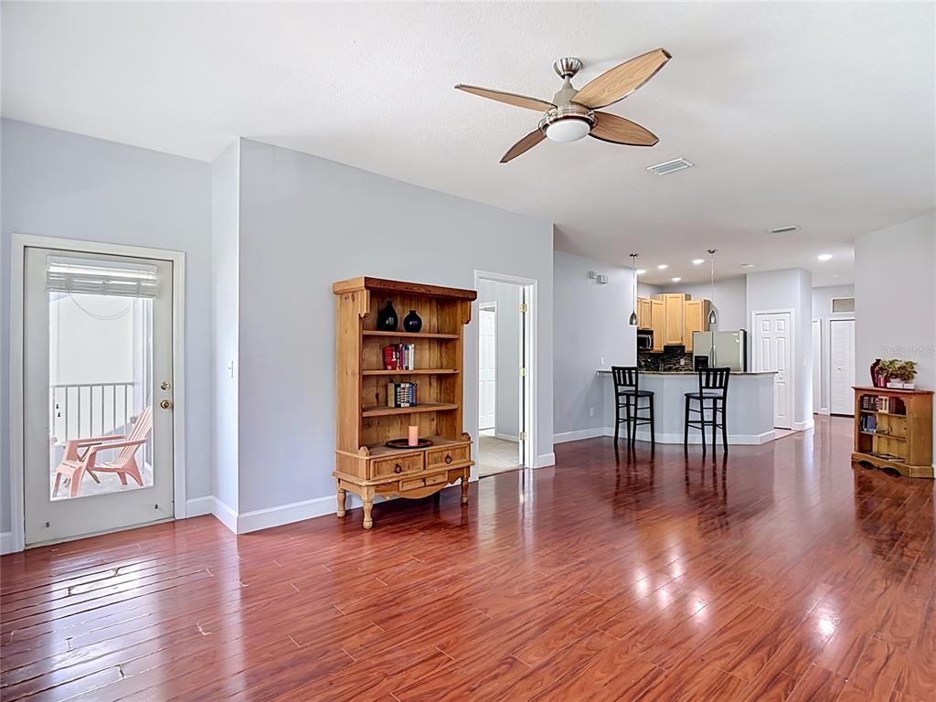 An open-concept living area features hardwood floors, a wooden bookshelf, and a kitchen with bar seating — 9502 W PARK VILLAGE DRIVE UNIT 108, TAMPA, FL