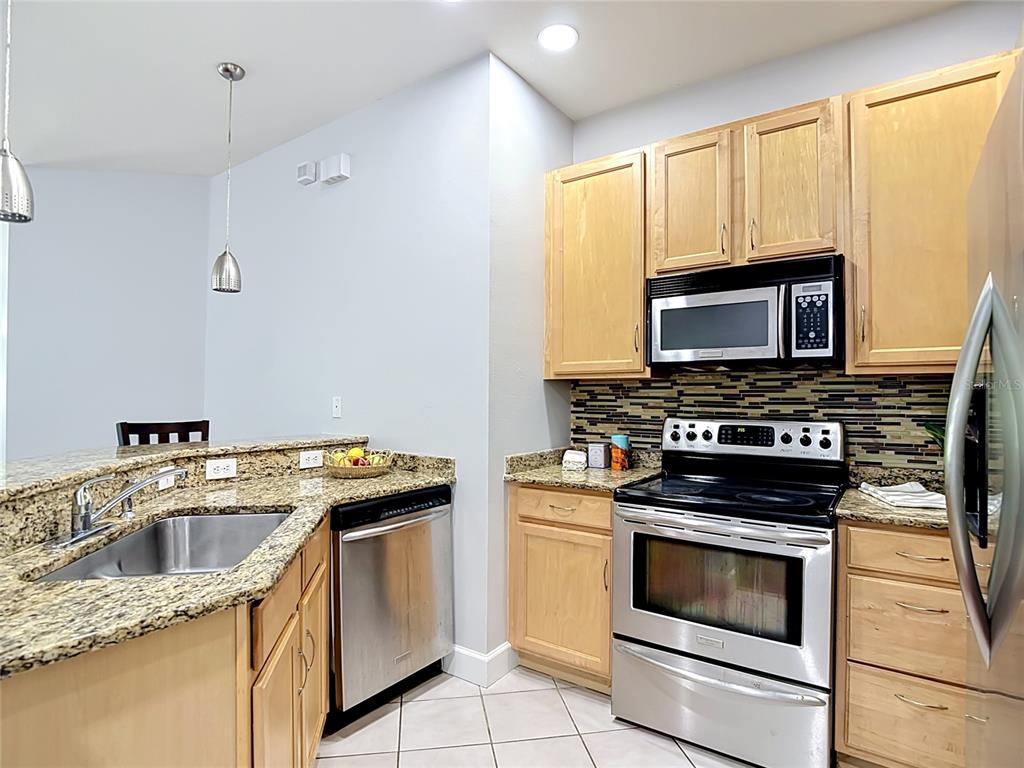 A kitchen features light wood cabinets, granite countertops, stainless steel appliances, and tile flooring — 9502 W PARK VILLAGE DRIVE UNIT 108, TAMPA, FL