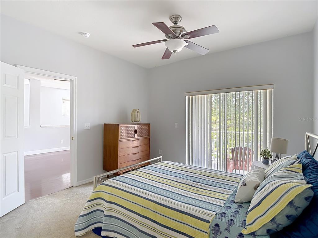 A bedroom with a striped bedspread, a wooden dresser, a ceiling fan, and sliding glass doors — 9502 W PARK VILLAGE DRIVE UNIT 108, TAMPA, FL
