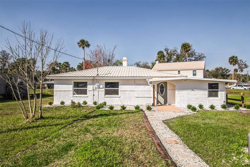 A single-story white house with a metal roof and a gravel walkway in the yard — 9400 NE 307TH COURT, FORT MC COY, FL
