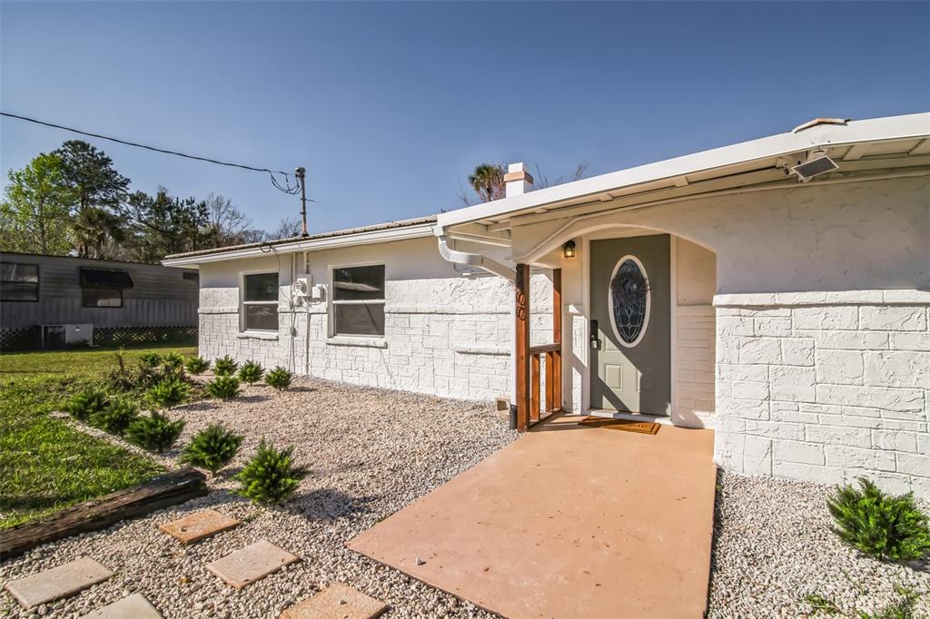 A white house with a textured stone facade, a gray front door, and gravel landscaping — 9400 NE 307TH COURT, FORT MC COY, FL