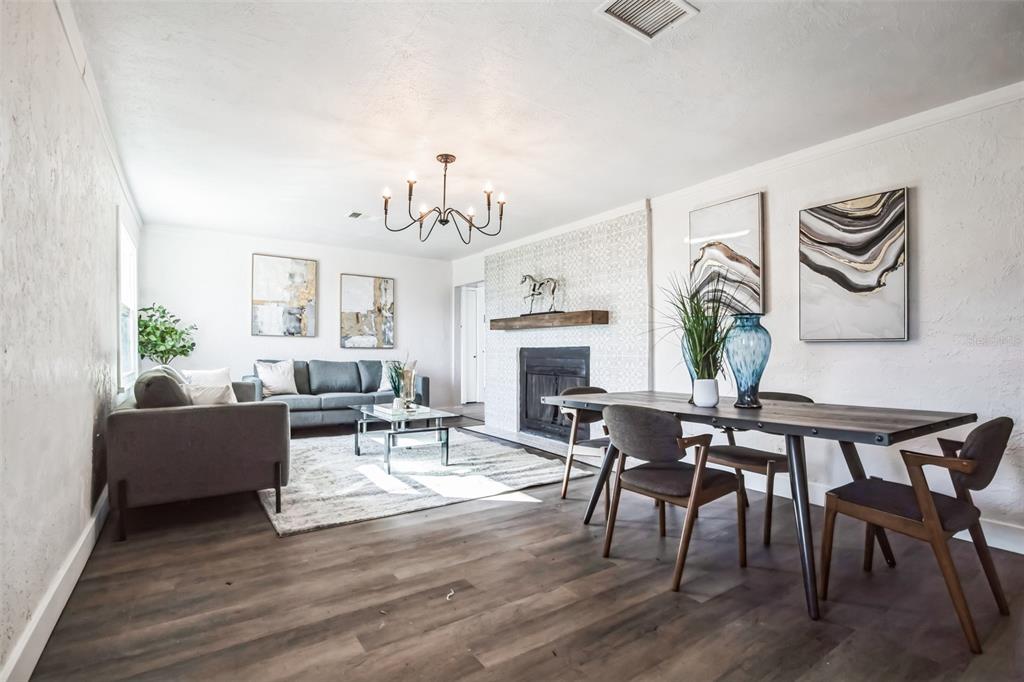 An open-concept living and dining room features a fireplace, chandelier, and wood-look flooring — 9400 NE 307TH COURT, FORT MC COY, FL