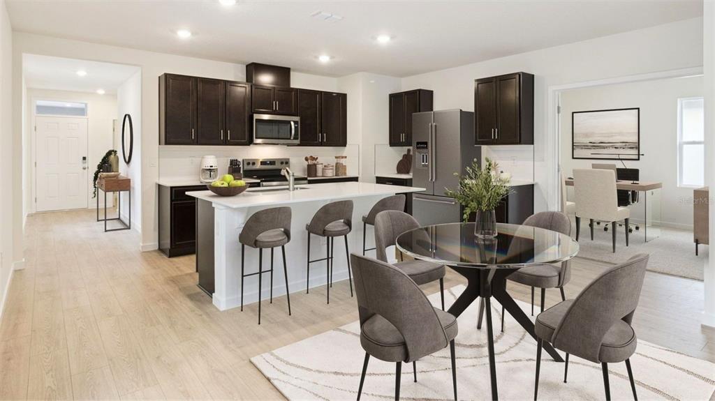 A modern kitchen features dark cabinetry, a white island with bar stools, and a dining area — 1917 HOWARD MESA DRIVE, KISSIMMEE, FL