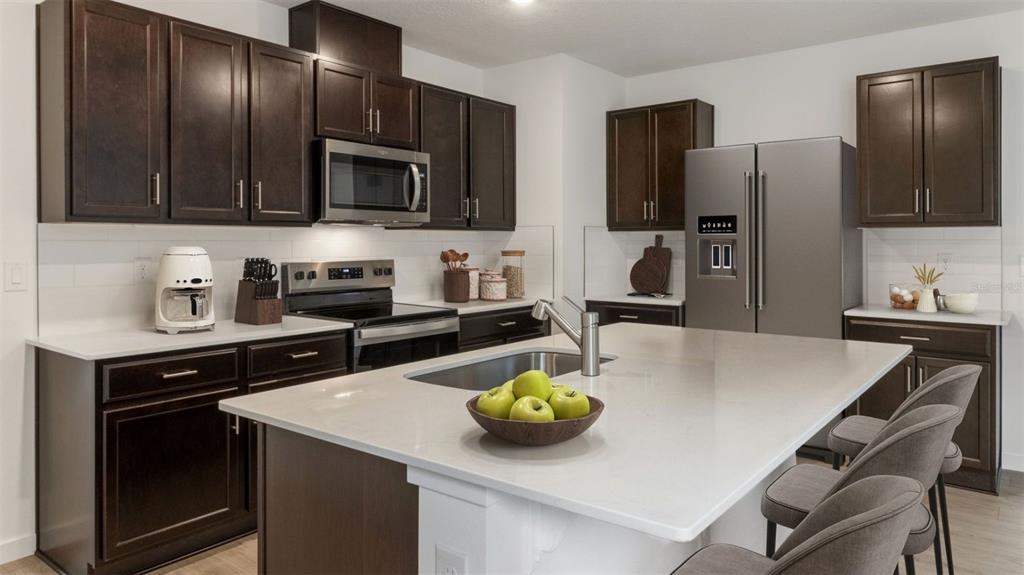 A modern kitchen features dark wood cabinets, stainless steel appliances, and a large quartz island — 1917 HOWARD MESA DRIVE, KISSIMMEE, FL