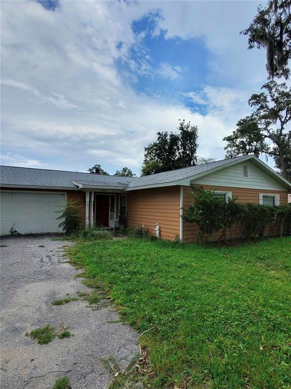 A single-story house with tan siding, a white garage door, and a grassy front yard — 3991 SE 19TH AVENUE, OCALA, FL