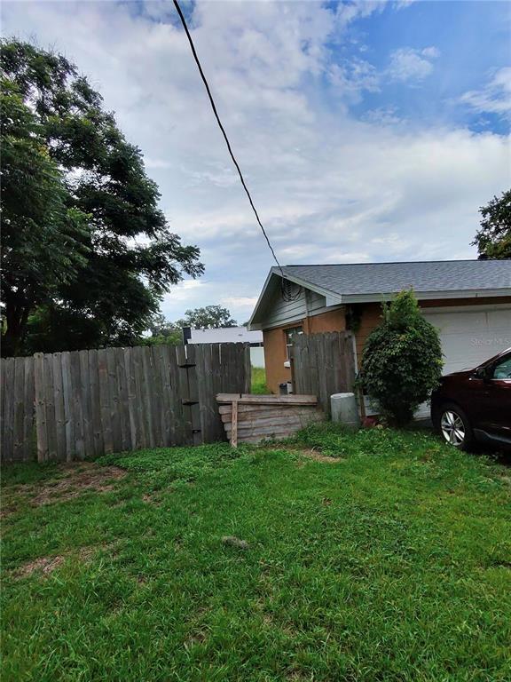 A wooden fence separates a grassy yard from a house with a partial view of a car — 3991 SE 19TH AVENUE, OCALA, FL