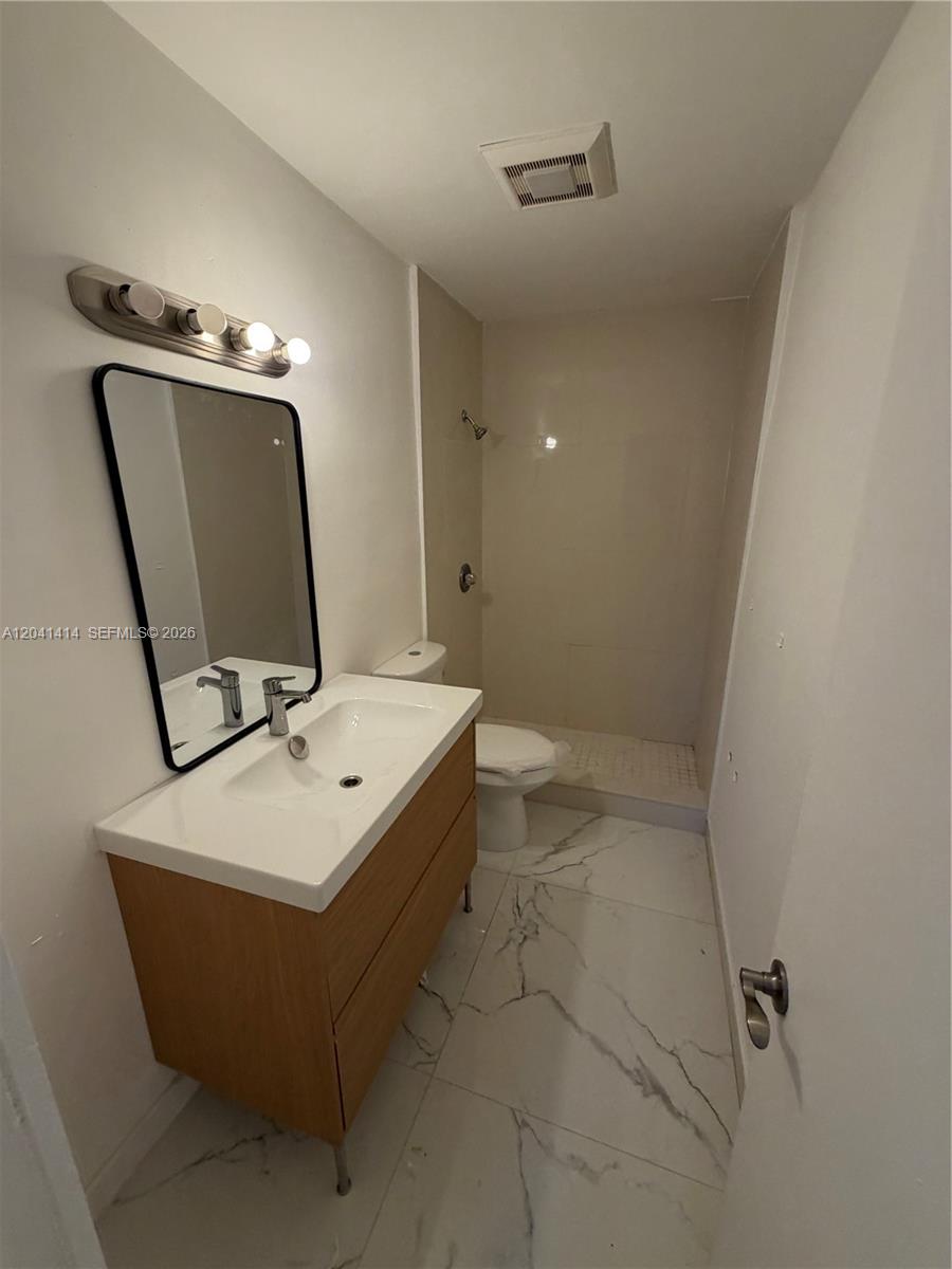 A bathroom features a wood vanity, a black-framed mirror, and white marble-patterned floor tiles — 2600 NW 112th St # 1, Miami FL 33167, MIAMI, FL