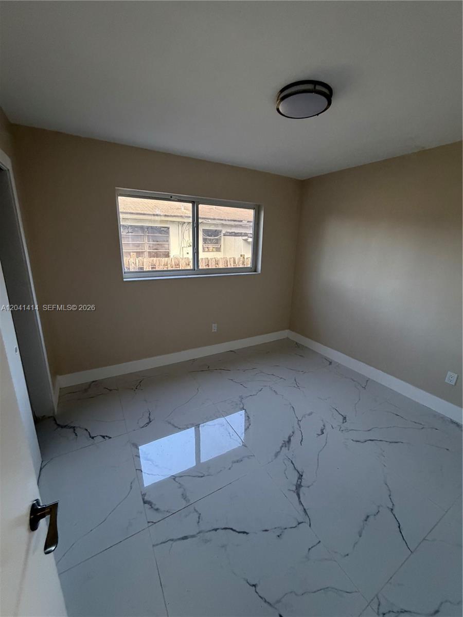 An empty bedroom features beige walls, a window, and white marble-patterned tile flooring — 2600 NW 112th St # 1, Miami FL 33167, MIAMI, FL