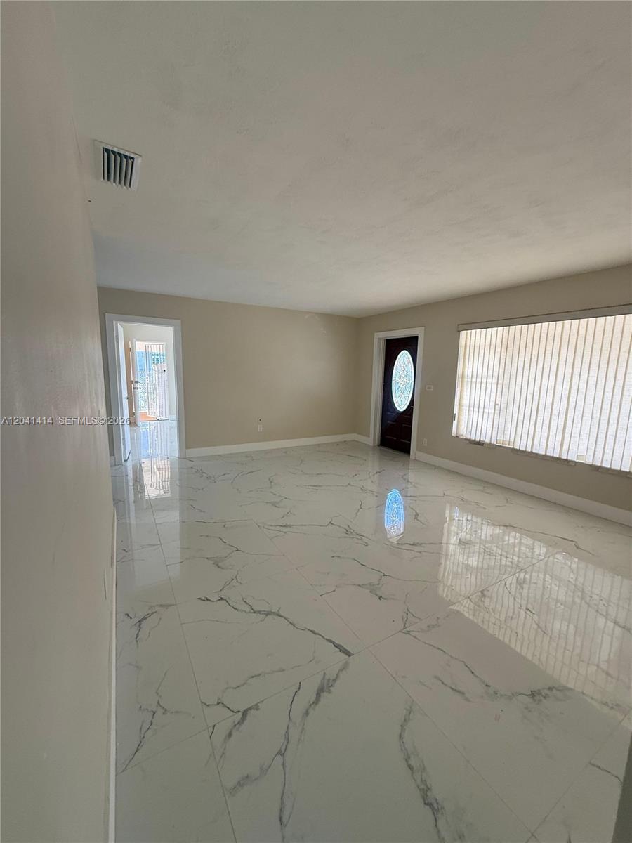 An empty room features white marble-look tile flooring, beige walls, and a dark front door — 2600 NW 112th St # 1, Miami FL 33167, MIAMI, FL