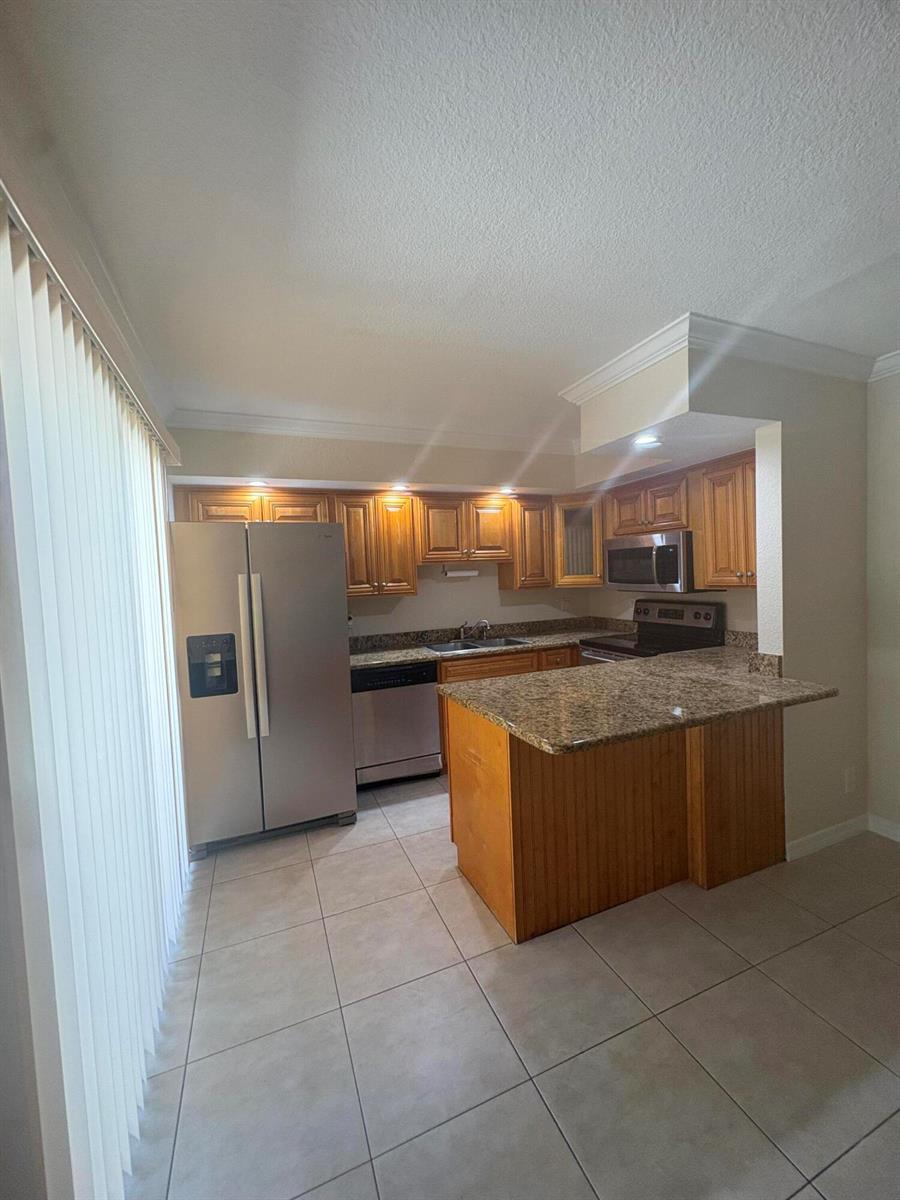 A kitchen features wood cabinets, granite countertops, stainless steel appliances, and a central island — 234 Lake Arbor Drive, Palm Springs FL 33461, PALM SPRINGS, FL