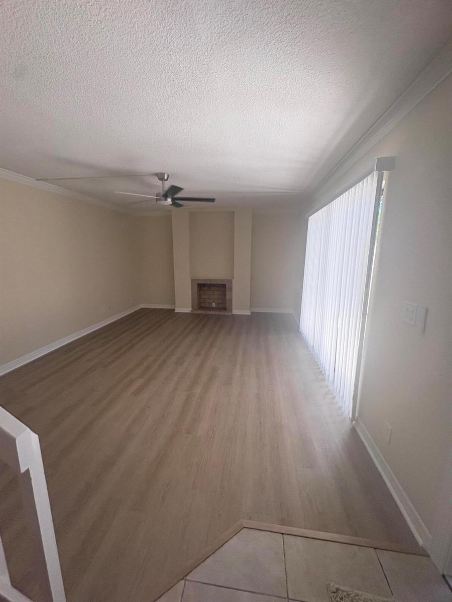 An empty living room features light wood-look flooring, a brick fireplace, and vertical window blinds — 234 Lake Arbor Drive, Palm Springs FL 33461, PALM SPRINGS, FL