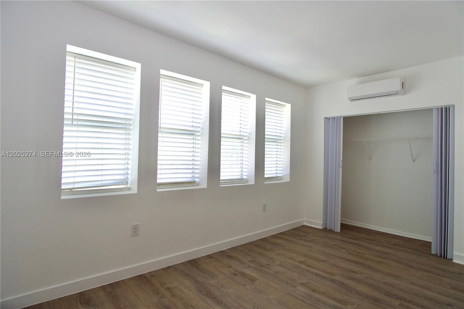 An empty room features white walls, wood-look flooring, four windows with blinds, and a closet — 501 SW 6th Ct # 213, Miami FL 33130, MIAMI, FL