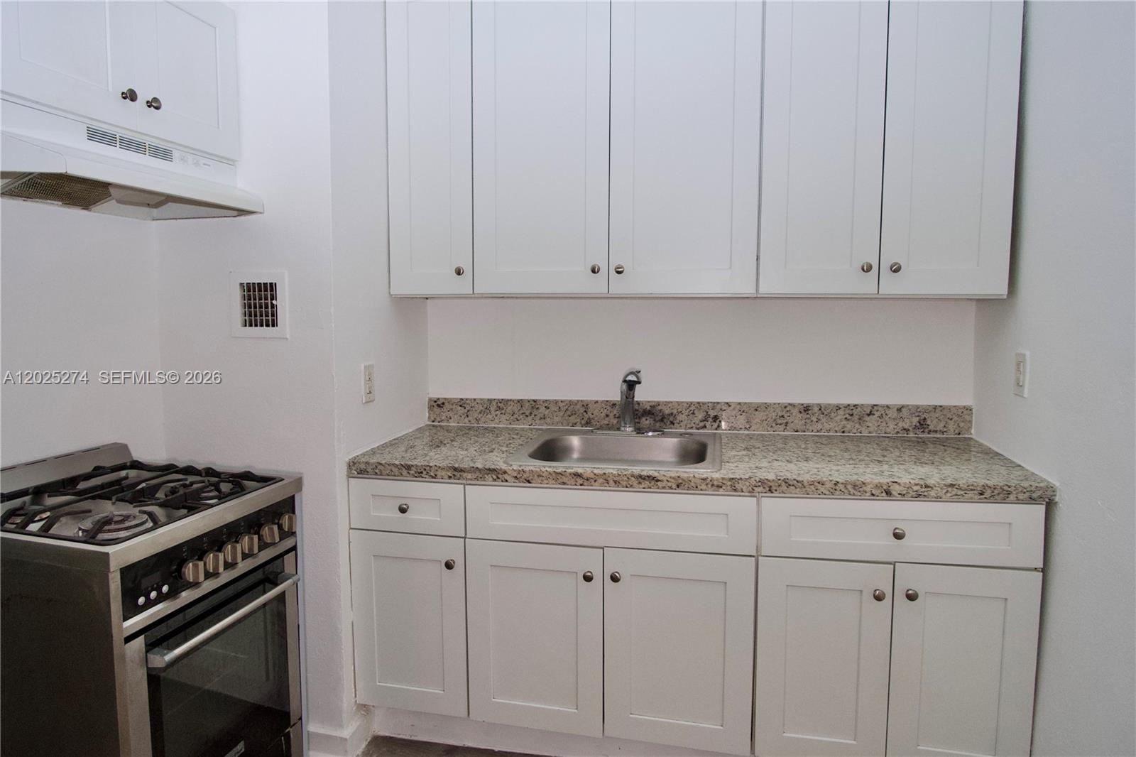 A kitchen features white cabinets, a granite countertop, a stainless steel sink, and a stove — 501 SW 6th Ct # 213, Miami FL 33130, MIAMI, FL