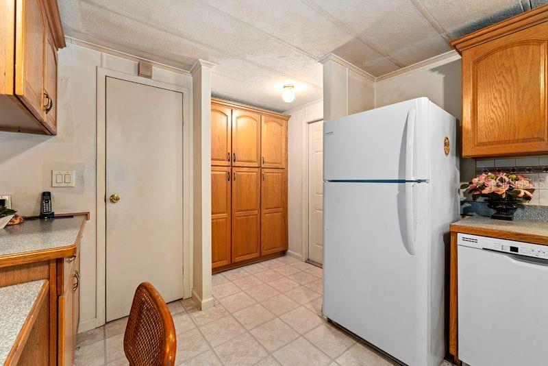 A kitchen features light-colored tile flooring, wood cabinets, a white refrigerator, and two closed doors — 9001 SHELDON WEST DRIVE, TAMPA, FL
