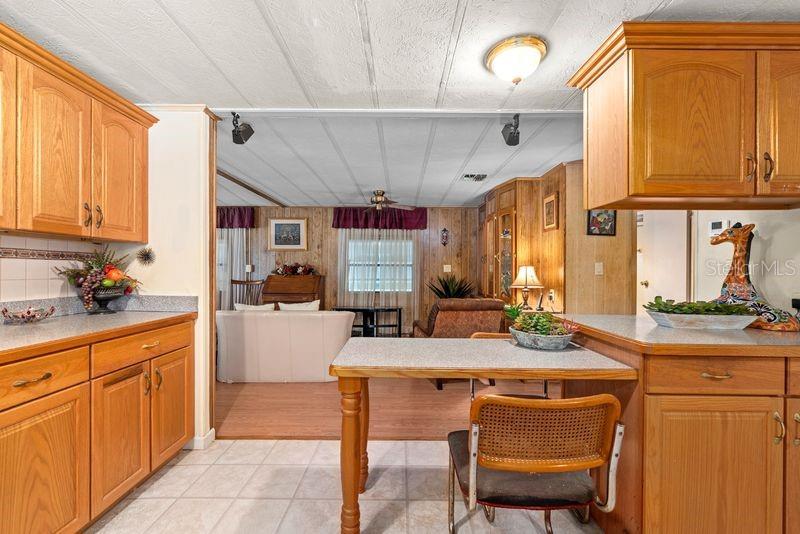 A kitchen with wood cabinets and a small dining table opens into a living area — 9001 SHELDON WEST DRIVE, TAMPA, FL
