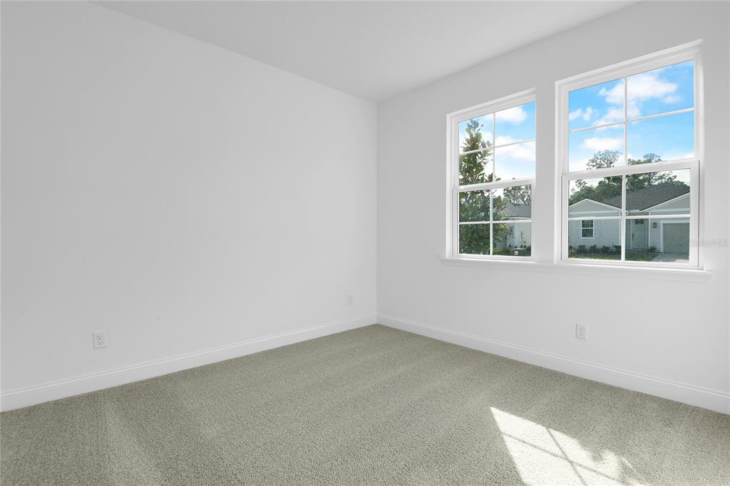 An empty bedroom with white walls, beige carpeting, and two windows overlooking a neighboring house — 195 ENCLAVE AVENUE, PALM COAST, FL